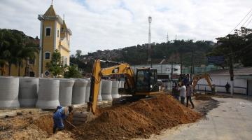 escavadeira e homem atuam em vala com tubos de concreto atrás #paratodosverem 