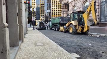 rua em obras com calçada à esquerda já coberta por pedras portuguesas. Há um trator na via. #paratodosverem 