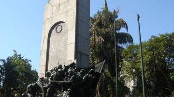 No centro uma praça com um monumento cercado por árvores - #paratodosverem