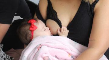 bebê é amamentado no peito. Mão olha para a criança. #paratodosverem