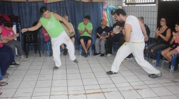 jovens fazem  movimentos de capoeira diante de roda de pessoas sentadas. #paratodosverem 