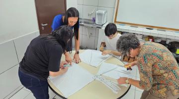 jovens mexem em papéis sobre uma mesa. #paratodosverem