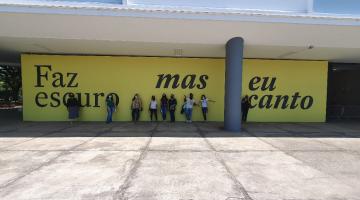 professoras em frente de painel escrito faz escuro mas eu canto #paratodosverem 