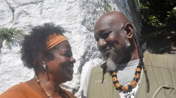 Casal de negros com bijuterias afro. Eles se olham. #Pracegover