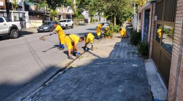 equipe de homens uniformizados capina meio-fio em rua. #paratodosverem 