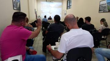 alunos estão sentados assistindo aula. Em primeiro plano, à esquerda, um aluno levanta a mão. #paratodosverem