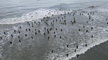 atletas estão entrando no mar. Imagem vista do alto, por drone. #paratodosverem