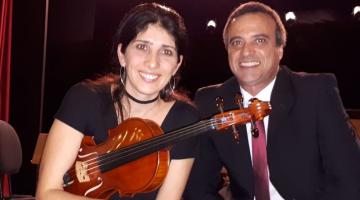 mulher e homem sentados e ela segura violino #paratodosverem
