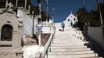 vista de nicho da Via Crucis à esquerda e trecho de escadaria com duas pessoas subindo. No alto, a capela. #paratodosverem