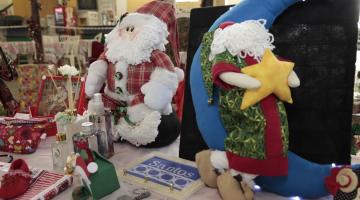 bonecos de papai noel e outros artigos de natal sobre uma mesa de exposição. #paratodosverem 