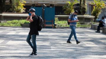 Homem está caminhando em praça e usando máscara. #Paratodosverem