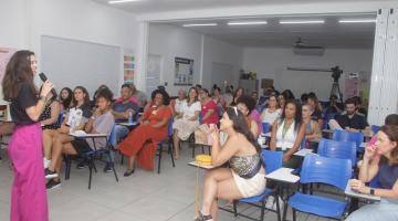 mulher dá palestra para outra mulheres que estão sentadas em uma sala. #paratodosverem 