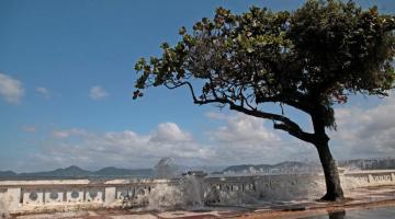 #PraCegoVer Imagem mostra ondas do mar penetrando pelos vão das muretas da orla