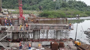 Grande estrutura de ferro rio adentro, com homens trabalhando. #Paratodosverem