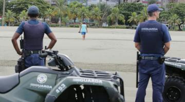 Dois guardas municipais estão na faixa de areia em pé e ao lado de quadriciclos. Á frente e distante, caminha um homem rumo ao jardim. #Paratodosverem