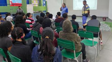 dois homens uniformizados da cet falam a jovens que estão sentados em pátio escolar. #paratodosverem 