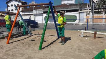 Operários pintam estrutura de balancê em playground. #paratodosverem