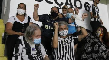 Rubens e José Roberto estão sentados lado a lado em cadeiras para assistir ao jogo. eles comemoram e sorriem com o gol marcado. Outras pessoas sentadas também comemoram. #paratodosverem