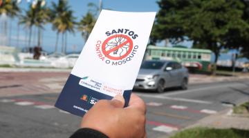 close de mão segurando folheto sobre aedes na orla. #paratodosverem