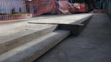 degraus e rampa em concreto em primeiro plano. No nível acima área tem uma cerca de plástico. #paratodosverem