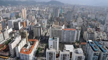 vista aérea de parte da Cidade com vário prédio e morros ao fundo. #Paratodosverem