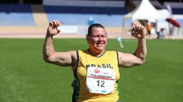 Beth gomes está com os braços abertos, em posição ângulo de 90 graus, com as mãos para cima e punhos fechados. #paratodosverem 