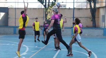 alexandre borgues está na quadra jogando basquete com adolescentes ele está segurando a bola e faz movimento de lance. Ele está de lado para a foto e seus dois pés estão fora do chão. #paratodosverem