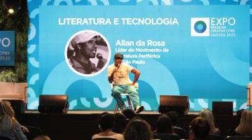 Allan da Rosa fala do microfone sentado. #paratodosverem