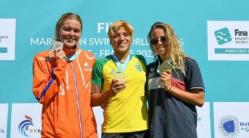 Ana Marcela e outras duas atletas exibem medalhas no pódio da prova. #pratodosverem