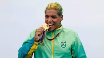 Ana Marcela 'morde' medalha de ouro vestida com uniforme da delegação do Brasil. #pracegover