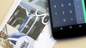 Smartphone está aberto em aplicativo de calculadora, sobre um carnê de IPTU. #Pracegover