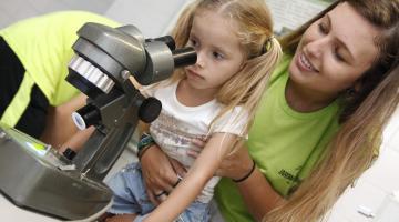 menina olha no microscópio ajudada por professora #pracegover 