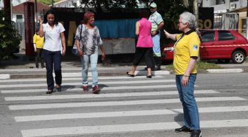 Agente da CET estende a mão mostrando a pessoas como atravessar a rua #paratodosverem