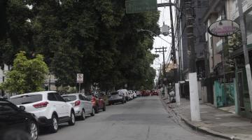 Trecho de avenida pavimentada, com veículos estacionados do lado esquerdo. #Pracegover