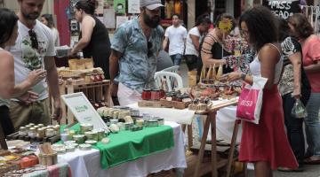 Estandes com objetos expostos em rua. Pessoas circulam pelo local 