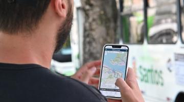 rapaz olha aplicativo com ônibus ao fundo #paratodosverem 
