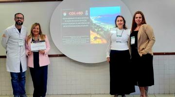 pessoas na frente de palco com tela em apresentação #paratodosverem 