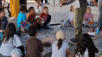crianças na atividade olham para monitor sentadas em círculo #paratodosverem 