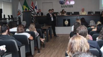 Auditório lotado de pessoas assistindo a uma palestra. Ao fundo, um homem fala ao público. #Pracegover