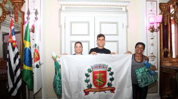 Os três atletas seguram bandeira da Cidade de Santos no salão nobre da prefeitura. #pracegover