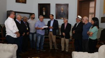 Prefeito entrega documento ao presidente da Câmara. Vários vereadores estão presentes e lado a lado na foto. #Pracegover