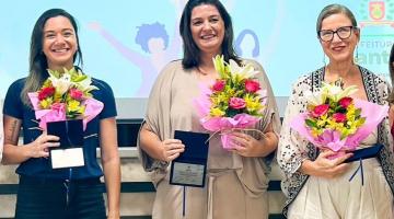 Rosane, Marilucy Fontes e Ingrid posam para foto segurando buquês de flores. #paratodosverem