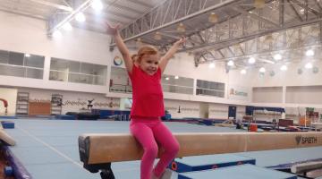 Criança com os braços estendidos em cima da trave de ginástica #paratodosverem