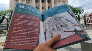 mão segura livro aberto em frente ao paço municipal. #paratodosverem