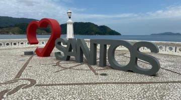 a escultura em um recuo na orla, com o coração em vermelho ao fundo e a palavra santos em cinza. #paratodosverem