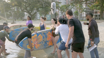 pessoas seguram prancha durante filmagem #paratodosverem