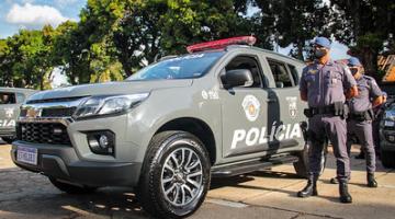 Viatura estacionada com dois policiais fardados ao lado. #pracegover