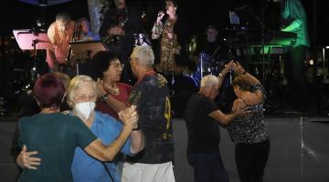 duplas danças no Baile na Praia ao som de banda que toda ao fundo num palco. #paratodosverem