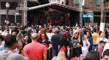 Público lota rua para assistir apresentação de banda em palco. #Pracegover