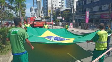 homens estendem a bandeira na rua preparando o hasteamento. #paratodosverem